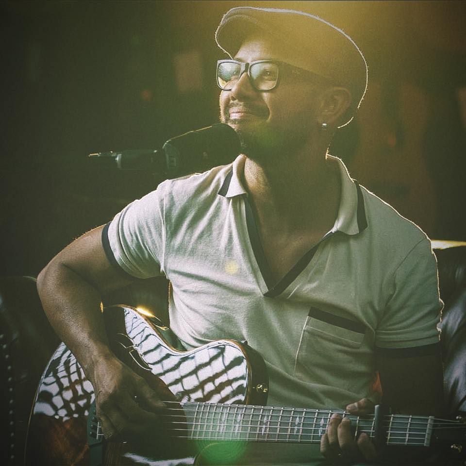 John Veloso playing guitar and smiling on stage